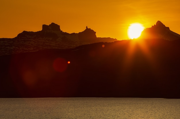 tramonto in montagne rocciose e riva del lago rosso arancione il sole tramonta dietro la catena montuosa della scogliera della siluetta