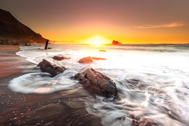 Tramonto mentre le onde del mare colpiscono le rocce sulla spiaggia della spiaggia di Ilbarritz a Biarritz Paesi Baschi