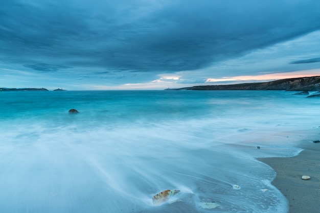 Tramonto nuvoloso sulla spiaggia di Arnao con onde moderate