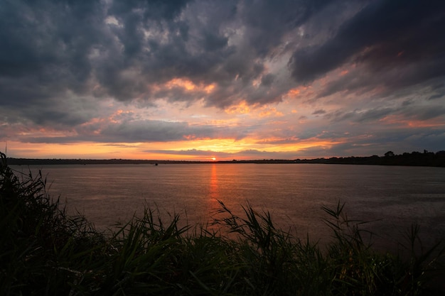 Tramonto sul fiume con canne in primo piano nuvole temporalesche