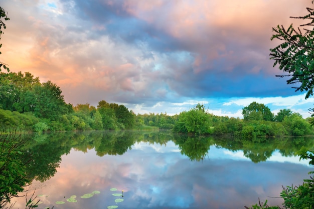 Tramonto sul lago con bosco verde e cielo colorato