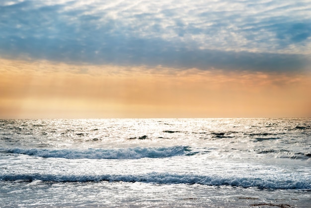 Tramonto sul mare blu con onde e nuvole drammatiche