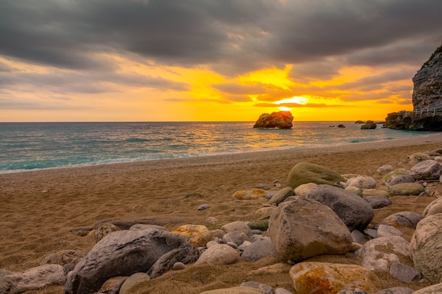 Tramonto sul mare e pietre su una spiaggia di sabbia