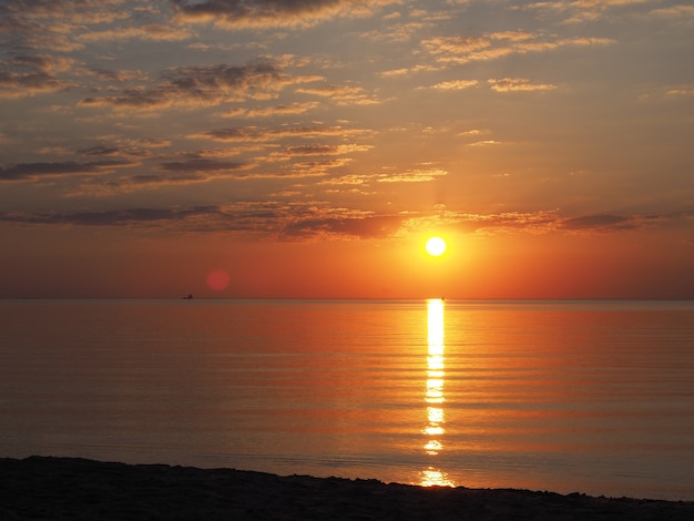 tramonto sulla costa del mare con sole arancione e riflesso in piccole onde e nuvole illuminate