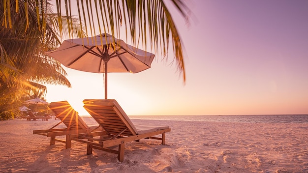 Tramonto sulla spiaggia tropicale come paesaggio estivo dell'isola con sedie ombrellone foglie di palma riva del mare calmo