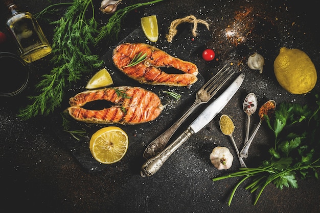 Trancio di salmone alla griglia con ingredienti limone, erbe aromatiche, olio d'oliva, tagliere in ardesia, tavolo arrugginito scuro