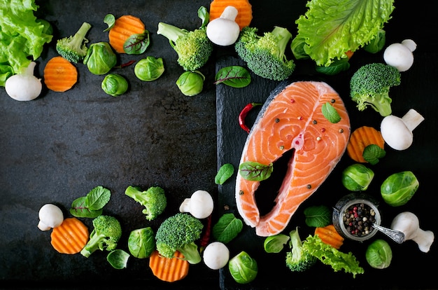 Trancio di salmone crudo e ingredienti per cucinare su una superficie scura in stile rustico. Vista dall'alto