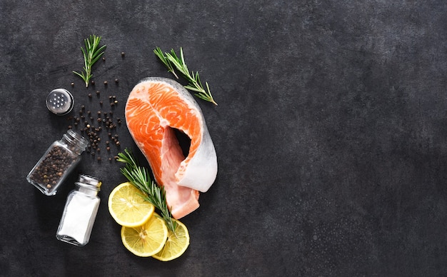 Trancio di salmone crudo, sale e rosmarino su uno sfondo nero concreto. Ingredienti per cucinare il pesce.