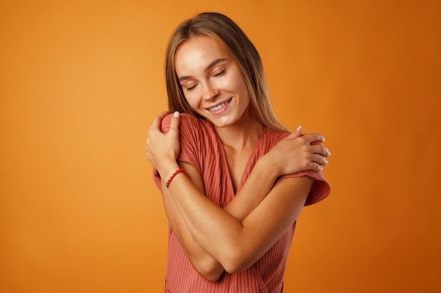 Tranquilla giovane donna bionda tenendo le mani sul petto su sfondo arancione.