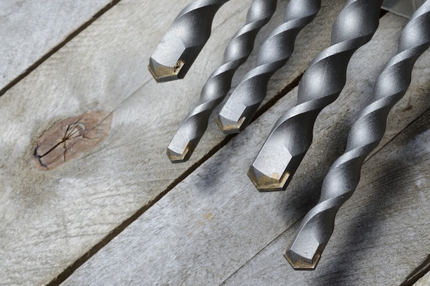 Trapani con punta in metallo duro per trapano a percussione giacciono su uno sfondo di legno della plancia. avvicinamento.