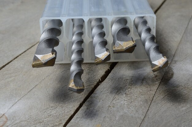 Trapani con punte per martello in metallo duro giacciono in una custodia di plastica su uno sfondo di legno della plancia. avvicinamento.