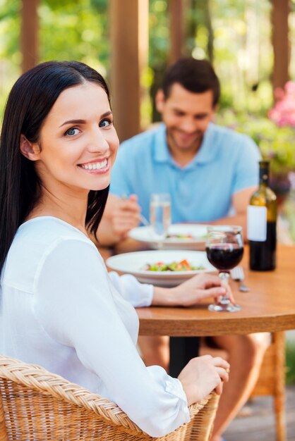 Trascorrere del tempo fantastico nel ristorante. Bella giovane coppia che si rilassa insieme nel ristorante all'aperto mentre la donna guarda la macchina fotografica e sorride