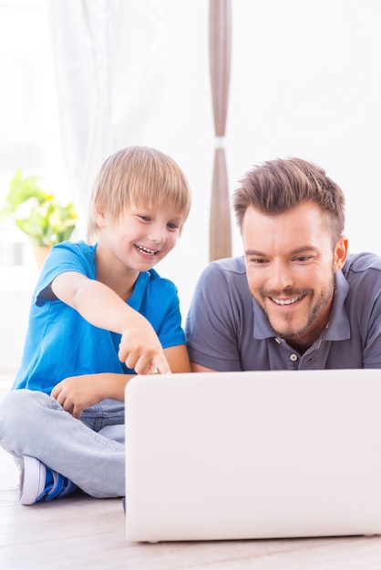 Trascorrere del tempo insieme. Felice padre e figlio che navigano in rete a casa mentre il ragazzino punta il monitor del laptop e sorride