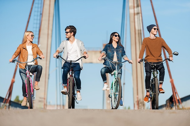 Trascorrere del tempo spensierato insieme. Quattro giovani in bicicletta lungo il ponte e sorridenti