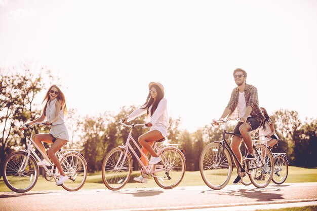 Trascorrere insieme una bella giornata estiva. Gruppo di giovani che vanno in bicicletta lungo una strada e sembrano felici