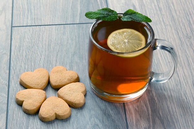 Trasparente tazza di tè con limone, menta e biscotti su un legno