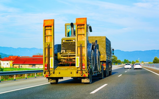 Trasportatore per auto con trattori su strada. Trasportatore di veicoli per auto a rimorchio basso su strada privata. Logistica dei trasporti europea al trasporto di lavoro di trasporto. Rimorchio per trasporti pesanti in autostrada.