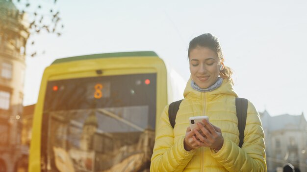 Trasporto pubblico urbano. Giovane donna alla moda che sta sulla stazione del tram che tiene gli smartphone e che aspetta tram