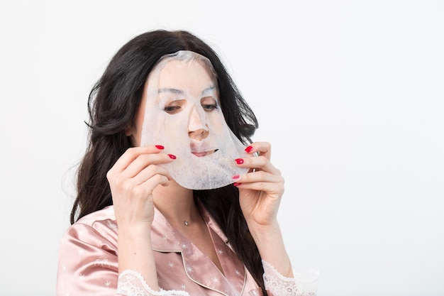 Trattamenti per la cura del viso e di bellezza Donna con maschera idratante in foglio sul viso isolata su sfondo bianco