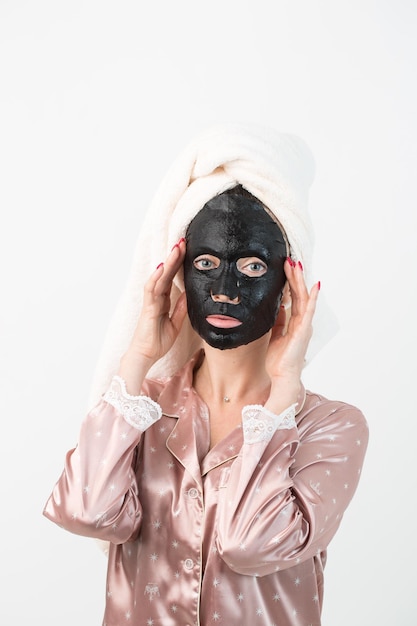 Trattamenti per la cura del viso e di bellezza Donna con una maschera al carbone idratante in foglio sul viso isolata su sfondo bianco