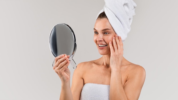Trattamenti per la cura della pelle Signora di mezza età con un asciugamano sulla testa che si guarda allo specchio