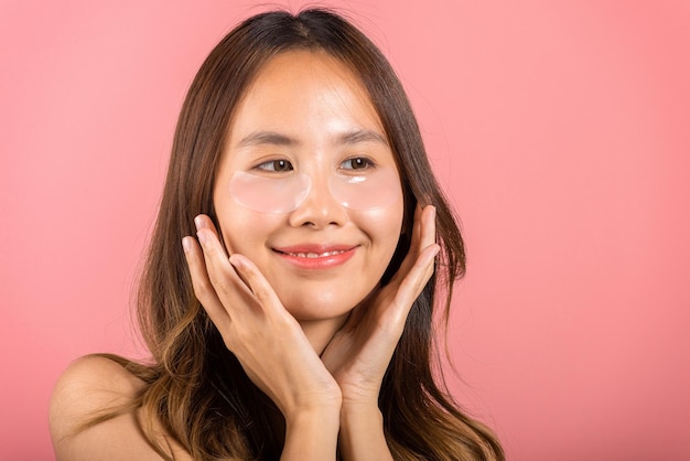 Trattamento della pelle degli occhi. Asiatica bella giovane donna maschera sorridente cerotti cosmetici gel sotto gli occhi, ritratto femminile con trucco naturale idrogel benda sull'occhio sul viso, isolato su sfondo rosa, cura della pelle