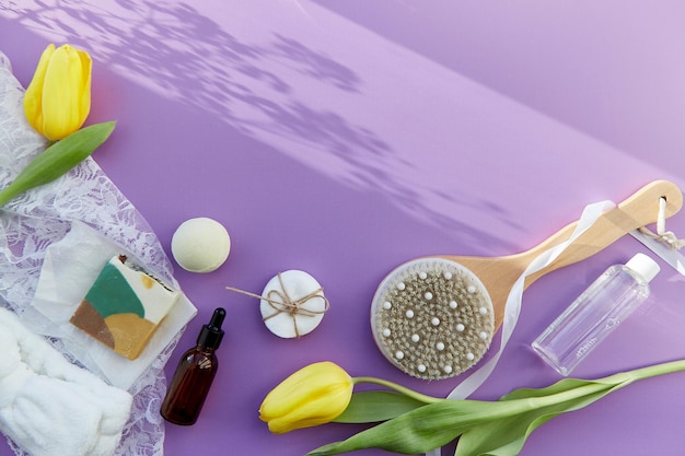 Trattamento di bellezza SPA completo di accessori per l'igiene sapone naturale essenza olio spazzola da massaggio bomba da bagno spugne su sfondo viola con tulipani Spazio di copia