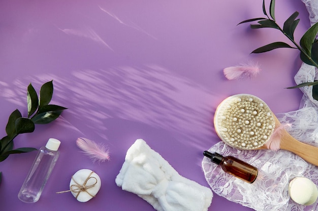 Trattamento di bellezza SPA con accessori per l'igiene essenza di sapone naturale spazzola per massaggio con olio da bagno spugne bomba su sfondo viola con fiori e ombre