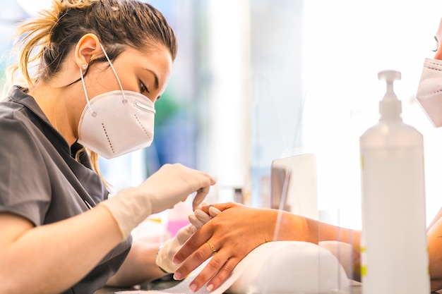 Trattamento di pedicure, lavoratrice bionda del salone di manicure e pedicure con misure di sicurezza e maschere per la riapertura della pandemia covida-19. Coronavirus