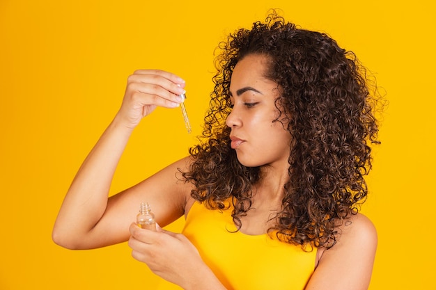 Trattamento riparatore delle doppie punte. Donna africana sorridente che spruzza olio essenziale sui suoi capelli castani ricci