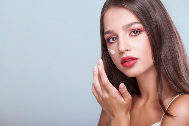 Trattamento viso. Donna con il viso sano, applicare la crema cosmetica sotto gli occhi