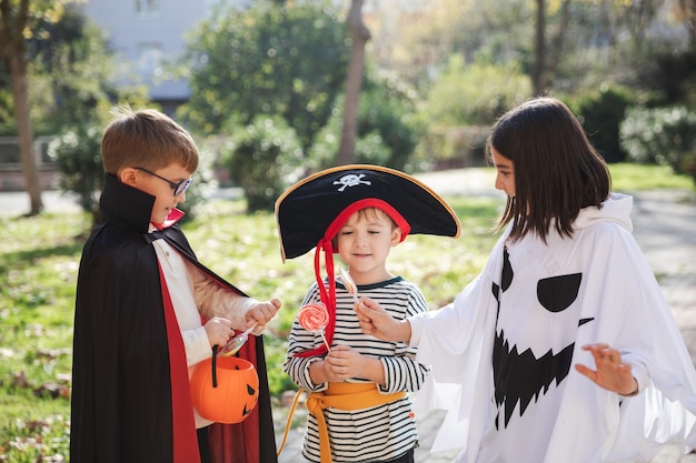 Trattare o ingannare Bambini felici che indossano costumi di carnevale di pirati fantasma e vampiri per la festa di Halloween condividendo caramelle tra loro che soggiornano nel parco