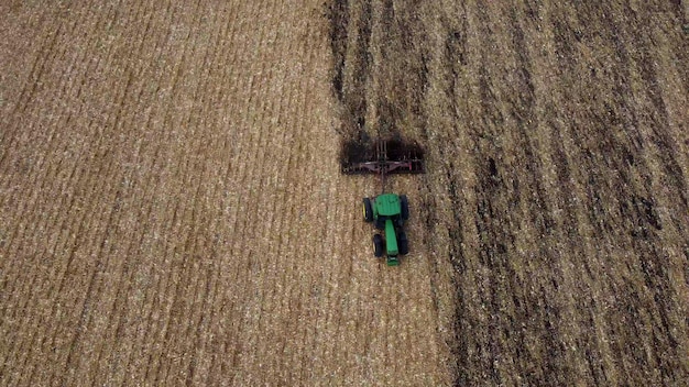 Trattore che ara il terreno sorvolando il trattore verde che ara il terreno nel campo giallo dopo harv