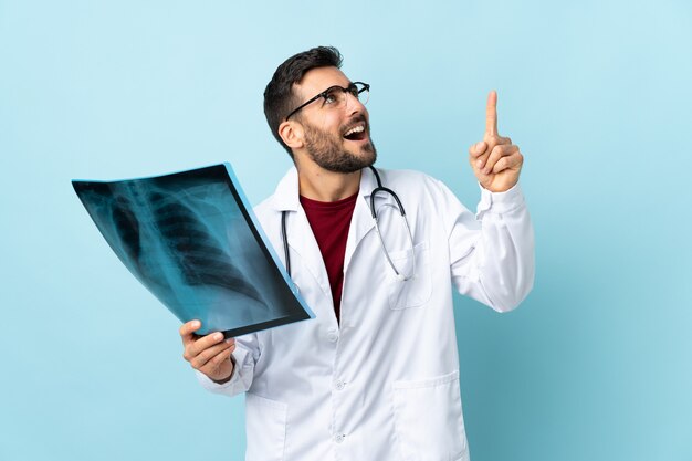 Traumatologo professionista che tiene la radiografia isolata sulla parete blu che indica con il dito indice una grande idea