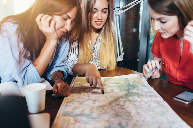 Tre amiche che pianificano la loro vacanza seduti al tavolo attorno alla mappa scegliendo la destinazione