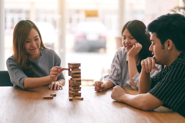 Tre amici asiatici seduti e giocando a un gioco di blocchi di legno della torre Tumble insieme sentendosi felici