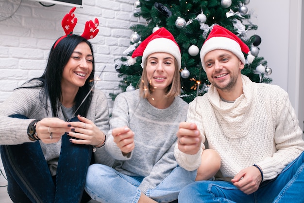 Tre amici con la scintilla che si siedono vicino all'albero di Natale