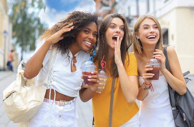 Tre amici di ragazze cool hipster alla moda bevono un cocktail sullo sfondo della città urbana