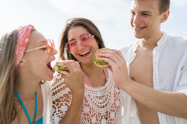 Tre amici felici all'aperto che godono insieme degli hamburger