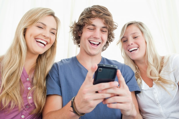 Tre amici guardando lo schermo di un telefono cellulare mentre sorridendo