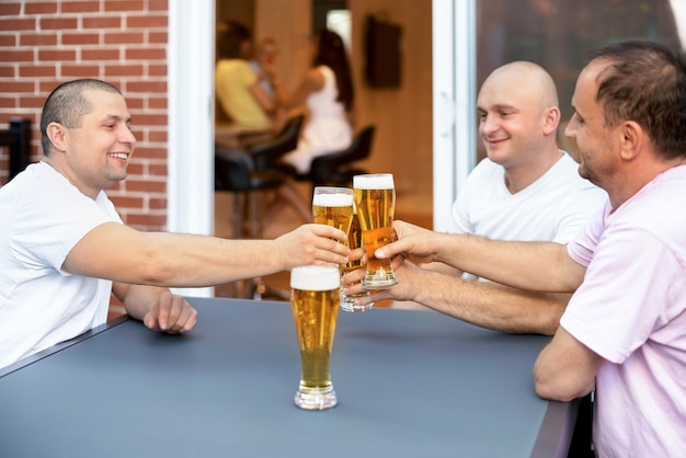 Tre amici maschii felici si rilassano bevendo birra fuori casa terrazza fuori casa.