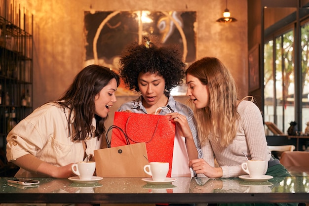 Tre amici multirazziali in una caffetteria che fanno regali per l'anniversario. Gente entusiasta che riceve regali.