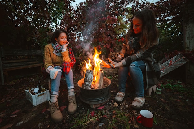 Tre amici si rilassano comodamente e bevono vino in una sera d'autunno all'aria aperta accanto al fuoco nel cortile sul retro