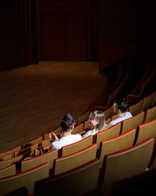 Tre amici una ragazza adolescente e due ragazzi sorridono guardando un film in un cinema vuoto con rosso