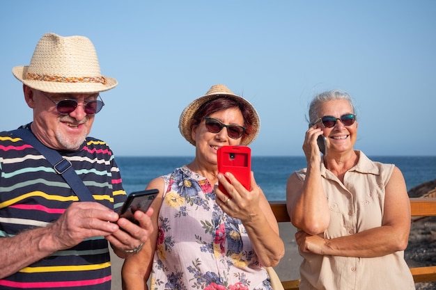 Tre anziani spensierati che utilizzano la messaggistica di chiamata sul cellulare mentre si godono la vacanza al mare