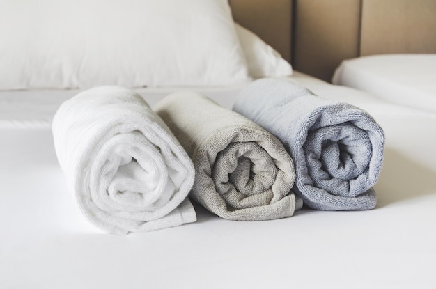Tre asciugamani da bagno freschi e puliti arrotolati in rotoli sul letto fatto di bianco nella camera d'albergo dopo la pulizia