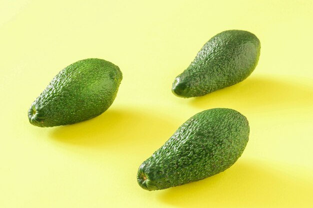 Tre avocado verdi maturi su sfondo giallo. Deliziosa verdura tropicale.