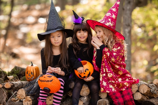 Tre bambine in costumi da strega di Halloween ridono evocano una passeggiata attraverso la foresta autunnale