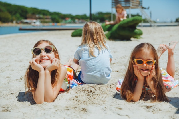 Tre bambini felici giacciono sulla sabbia sulla spiaggiaun bambino con sindrome di down con gli amici si diverte sulla spiaggia