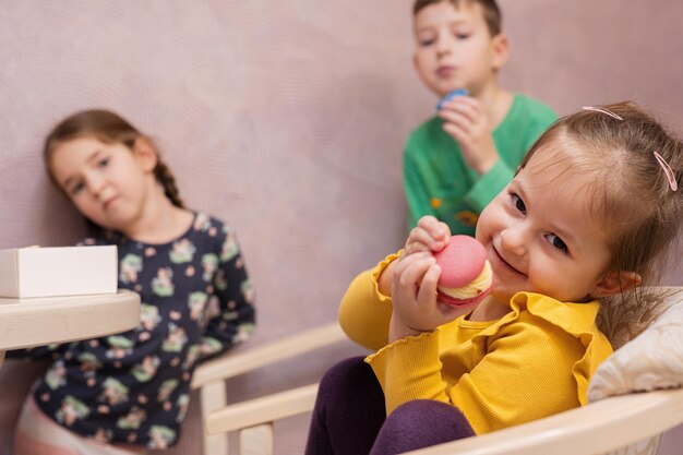 Tre bambini mangiano deliziosi e gustosi macarons dai colori dolci